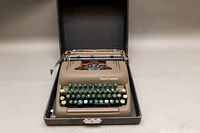 Full view of typewriter in case showing brown body, green and white keys.