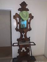 Full view of the antique wooden hall tree showing carved design, mirror with green hat, and general shape