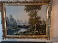 Full view of the large canvas painting with a landscape scene framed in an ornate gold frame
