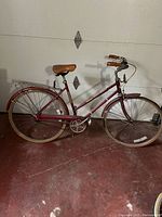 Right side view of maroon vintage ladies bike showing frame, saddle, rear rack, wheels, and pedals.