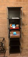Front view of the black wood and silver metal 5 shelf bookcase showing instruction booklet on one shelf and some contents (not included).
