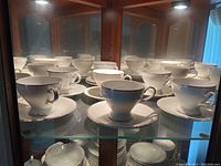 Wide shot of china cups and saucers arranged in cabinet showing the set's style and condition