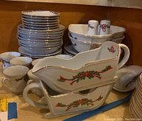 Stacked dinner plates, several bowls, creamer, salt and pepper shakers, gravy boat and rectangular serving dishes, all decorated with Christmas poinsettia and ribbon pattern with gold trim.