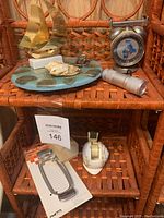 View of whole lot including brass ship model, ceramic trivet with shells, retro metal timer, handheld butter cutter in package, and ceramic tape dispenser.