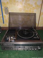 Front view photo of Emerson stereo console showing turntable, control panel, AM/FM tuner, 8-track player, and cassette recorder. Microphone and replacement needle visible.