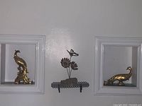 Two gold gilded Syroco figurines resembling stylized peacocks placed on a wall with decorative molding.