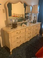 Front view of the French Provincial dresser with nine drawers and matching mirror on top. Shows the off-white finish and ornate gold drawer pulls.