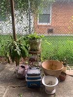 Outdoor shot showing live garden plants in various pots placed on and around a vintage metal plant stand, small cooler in front, and ceramic planters grouped together.