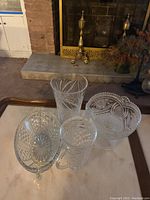Five crystal glassware items including a tall vase and four bowls with intricate cut designs, displayed on a wooden surface in front of a fireplace.
