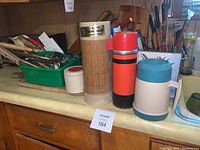 Three vintage Thermos containers in different colors alongside kitchen utensils and cutting boards.