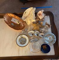 Photo showing overall lot with the shells, starfish, copper bowl, porcelain plates, glass ashtray, and perforated bowl on a white marble table top.