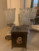 Photo showing two clear Bohemia glass hurricane candle lamps on marble bases with a vintage floral metal tissue holder and coasters placed in front.
