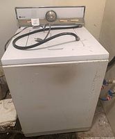 Front view of white upright washer showing general condition with rust and wear, power cord on top.