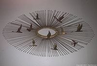 Front view of the full metal wall art item showing sunburst design with birds flying around an oval center