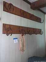Full view of two wooden shelves mounted on wall with multiple horseshoe hooks for hanging items.