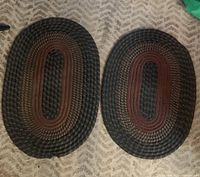 Two braided oval floor rugs side by side on a carpet. Larger rug on the left and smaller on the right, showing overall condition and size difference.