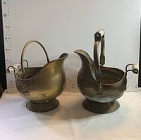 Pair of vintage brass coal scuttles with porcelain handles shown side by side from the front
