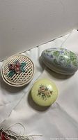 Three yellow alabaster trinket boxes: egg-shaped with floral design, round basket weave with pink roses, and small round floral box.