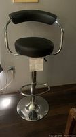 Front view of a single adjustable bar stool with black padded seat and backrest, chrome frame and base.