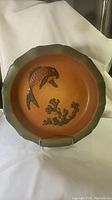 Top view of round ceramic dish with scalloped dark green rim and orange center featuring raised fish and coral reliefs.