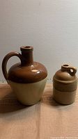 Two ceramic jugs, the larger Bourne Denby jug on the left with brown and beige glaze, and the smaller Canadian Whiteoak jug on the right with beige and brown glaze