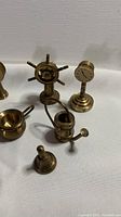 Close-up of several brass miniatures including a ship's wheel, clock on pedestal, watering can, and small brass items on white background