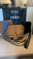 Photo showing three different front panels for Coco and Carmen crossbody bags placed on a surface with the branded dust bag behind them.