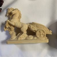 Side view of beige resin figurine showing a detailed horse rearing up and ornamental Roman chariot.