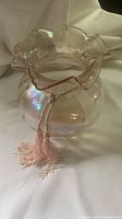 Front angled view of the pink iridescent glass flower-shaped bowl with ruffled edges and pink tassel on a white background.