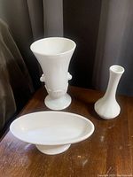 Photo of three milk glass pieces: tall urn with handles, pedestal bowl on a foot, and slender vase.