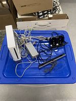 Wii console with power adapter, sensor bar, and charging dock on a blue container.