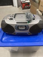 Front view of Philips Magnavox AZ1207 boombox showing speakers, control panel, and CD player lid with remote control on top