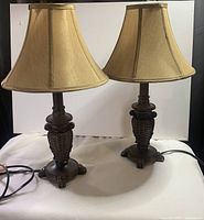 Pair of small table lamps with beige fabric shades and ornate dark bronze textured bases with claw feet, shown side by side.