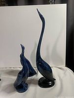 Front view of three blue bird pottery sculptures with tall bird on right and two smaller birds on left.