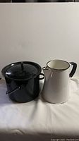 Photo showing both the vintage black speckled enamel pot with lid and the white enamel pitcher side by side.