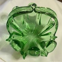 Top angle view of the vintage green glass basket showing the handle, bulging decorative rim, and textured base.