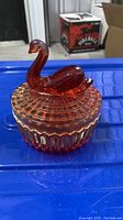 Photo showing the amberina red pressed glass swan bowl from side angle on blue surface.