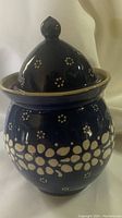 Side view of vintage Polish pottery jar with lid on, showing blue glaze and white floral pattern, beige rim.