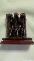 Front view of maroon antique resin three wise monkeys figurine on base