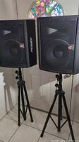 Two black Peavey SP 112MX speakers mounted on On-Stage tripod stands, front view