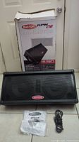Photo of the Kustom KPM210 PA monitor speaker with the original box behind it, also showing the user manual and power cable on the floor in front.