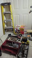 Full view showing Husky step ladder, boxed Skil circular saw, tool bags and assorted tools on floor.