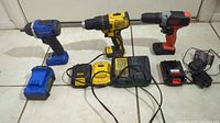 Wide view showing all three drills with their batteries and chargers on a tiled floor.