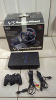 Sony PlayStation 2 console with accessories and V3 Racing Wheel box in background