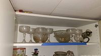 Photo of crystal stemmed glass goblets, pitcher and serving bowls arranged on white shelf
