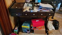 Front view of dark wood desk showing five knobs on drawers and storage space underneath with various boxes and clutter surrounding it.