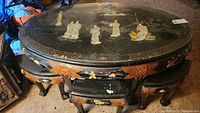 Oval Japanese dining table with black lacquer, glass top, carved edges with gold accents, four nesting stools underneath.