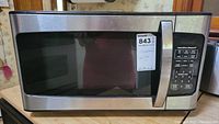 Front view of Hamilton Beach microwave oven showing its stainless steel body, black glass door, and control panel label with model info and auction sticker.