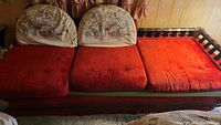Front view of red velvet sofa with three seat cushions and two rounded floral patterned back cushions.