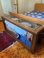 Sofa table showing wooden frame with glass top and storage area underneath filled with various items not included in lot.